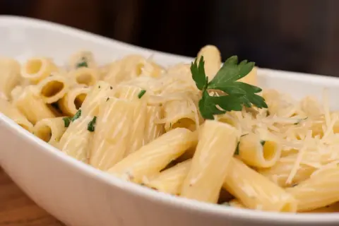 Pyszny makaron z parmezanem, udekorowany natką pietruszki, w białej misce.