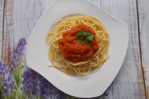 Spaghetti ze świeżych pomidorów, udekorowane natką pietruszki, na białym talerzu, na tle drewnianego blatu i lawendy.