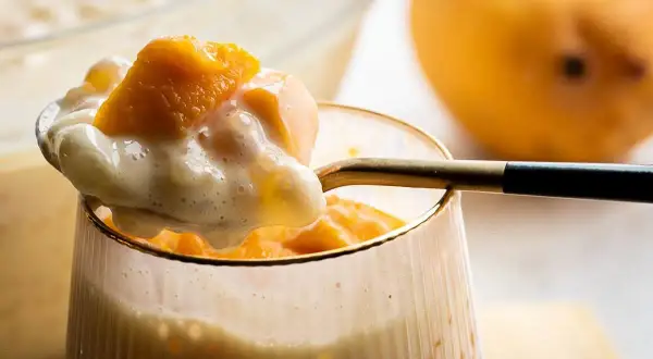 Słodkie monoporcje mango z kremowym deserem, podane w szklance. Obok leży dojrzałe mango.