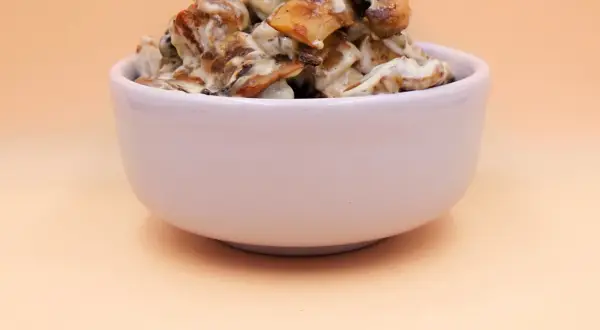Tofu z pieczarkami w kremowym sosie, podane w białej miseczce.
