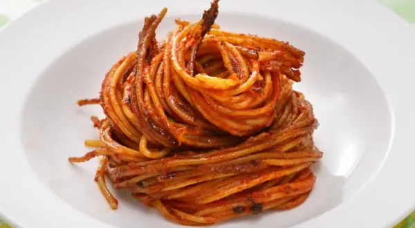 Spaghetti all'assassina, lekko przypieczone, w intensywnym sosie pomidorowym, ułożone na białym talerzu.