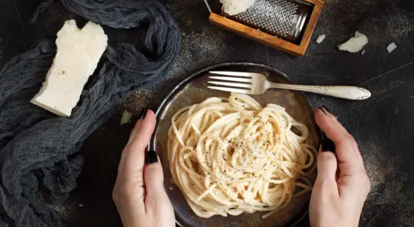 Idealny ser do spaghetti? Ten parmezan starty na tarce i kawałek obok talerza z makaronem sugerują odpowiedź.