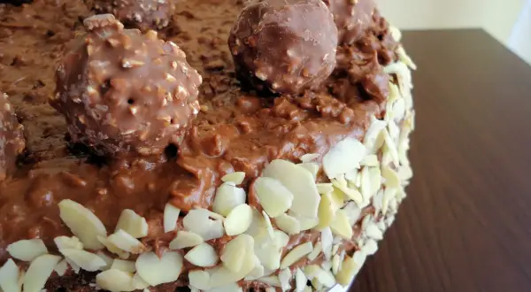 Pyszny tort Ferrero Rocher, obficie udekorowany czekoladowymi kulkami i płatkami migdałów.