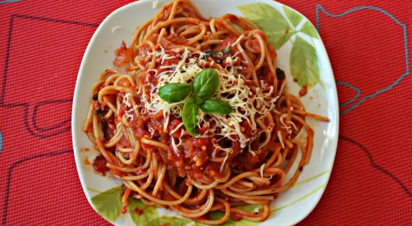 Pyszne spaghetti z pomidorami, posypane startym serem i udekorowane listkami bazylii. Idealne na szybki obiad.