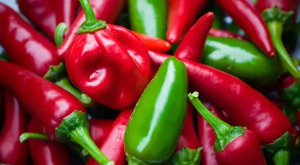 Stos czerwonych i zielonych papryczek chili, w tym jedna okrągła czerwona papryczka.