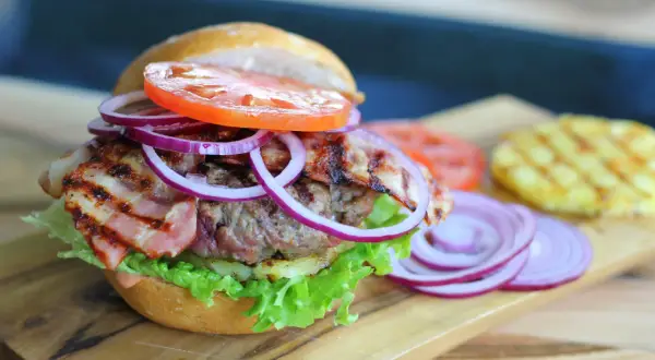 Pyszny, małomiasteczkowy burger z soczystą wołowiną, chrupiącym boczkiem, świeżą sałatą, pomidorem i czerwoną cebulą.
