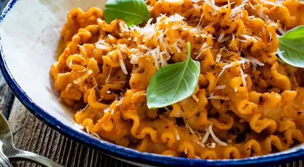 Pyszna włoska pasta z sosem pomidorowym, posypana parmezanem i udekorowana listkami bazylii. Idealna na obiad.