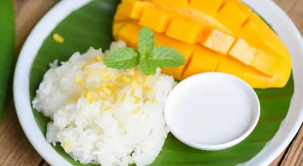 Pyszny mango sticky rice: soczyste mango, kleisty ryż, mleczko kokosowe i listek mięty na liściu bananowca.