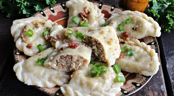 Pyszne pierogi z kaszą gryczaną i serem białym, okraszone skwarkami i szczypiorkiem, na ozdobnym talerzu.