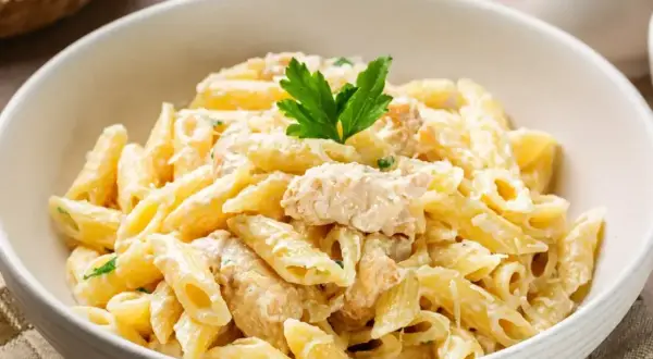 Pyszne danie z makaronem penne w kremowym sosie z kurczakiem, udekorowane natką pietruszki.