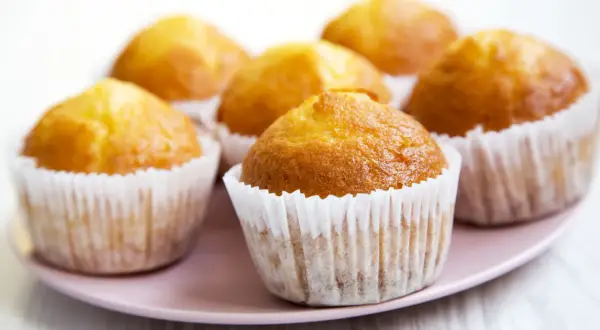 Kilka apetycznych, zdrowe muffinki w papierowych foremkach na różowym talerzu.