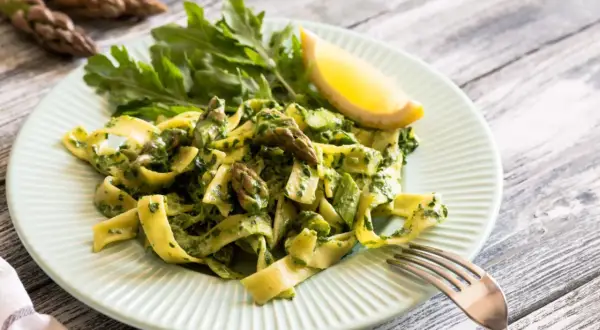 Pyszny makaron ze szparagami i zielonym pesto, udekorowany cytryną i rukolą. Idealne danie na wiosnę.