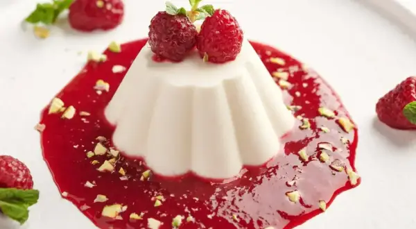 Panna cotta przepis: aksamitny deser z malinowym sosem, pistacjami i świeżymi malinami. Idealny na letnie popołudnie.