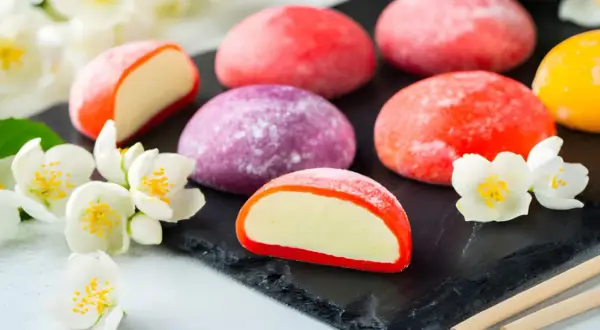 Kolorowe japońskie desery mochi, otoczone białymi kwiatami jaśminu, kuszą swoim wyglądem i smakiem.