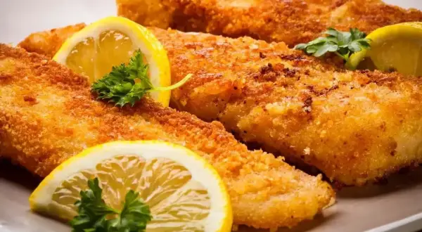 Chrupiące filety rybne w panierce panko, ozdobione plasterkami cytryny i natką pietruszki, kuszą apetycznym wyglądem.
