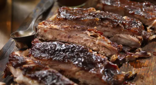 Soczyste żeberka w piwie, polane gęstym sosem BBQ, prezentują się apetycznie na drewnianej desce.