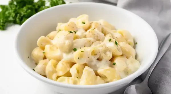 Miseczka kremowego mac and cheese, posypana natką pietruszki, obok łyżka i zielona gałązka.