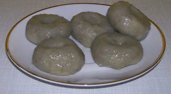 Pięć okrągłych, szarych klusek śląskich z charakterystycznym wgłębieniem na talerzyku.