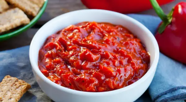 Pyszna, domowa pieczona papryka po bułgarsku w białej miseczce, obok chrupiące krakersy i świeże papryki.