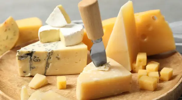 Różnorodne rodzaje serów: pleśniowy, camembert, parmezan i żółte sery, ułożone na drewnianej desce, gotowe do degustacji.
