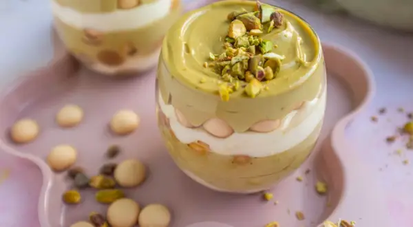 Pyszne tiramisu pistacjowe w szklance, przełożone kremem i biszkoptami, posypane posiekanymi pistacjami.