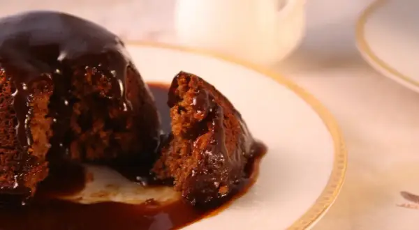 Pyszny, wilgotny deser sticky toffee, polany gęstym, karmelowym sosem, na eleganckim talerzyku.