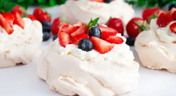 Mini bezy Pavlova z bitą śmietaną, truskawkami i borówkami. Delikatne, chrupiące na zewnątrz i miękkie w środku.