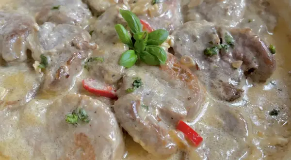 Soczyste polędwiczki w kremowym sosie camembert, udekorowane listkami bazylii i kawałkami papryki. Pyszne danie gotowe do podania.