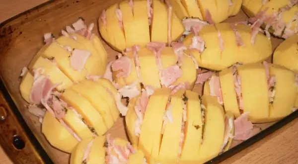 Ziemniaki hasselback z boczkiem i serem, gotowe do pieczenia w naczyniu żaroodpornym.