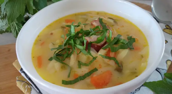 Aromatyczna zupa słodko kwaśna z kawałkami kiełbasy, ziemniaków i marchewki, udekorowana świeżymi ziołami.
