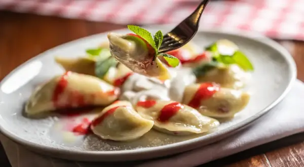 Jak gotować mrożone pierogi? Na talerzu pyszne pierogi z polewą truskawkową i miętą.