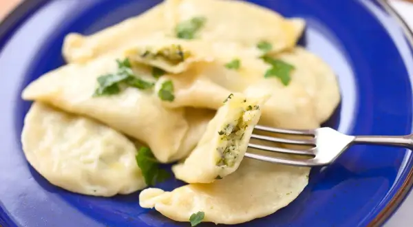 Pyszne pierogi ze szpinakiem i serem, udekorowane natką pietruszki, czekają na widelcu.
