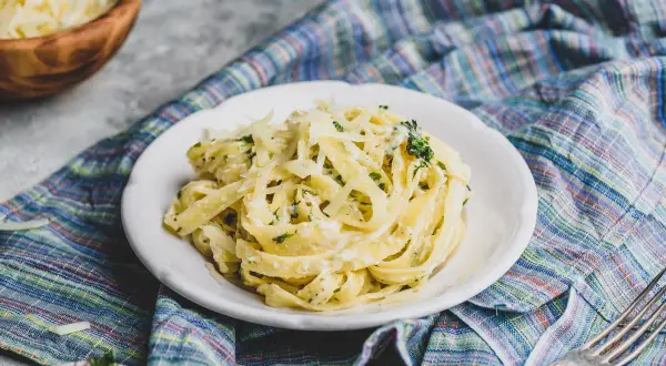 Pyszne fettuccine alfredo, bogato posypane parmezanem, na talerzu z kolorową serwetką.
