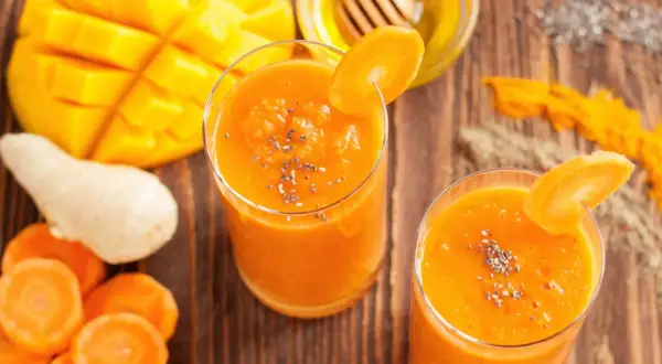 Dwa szklanki pomarańczowego koktajlu z mango i marchewki, ozdobione plasterkiem marchewki i nasionami chia.