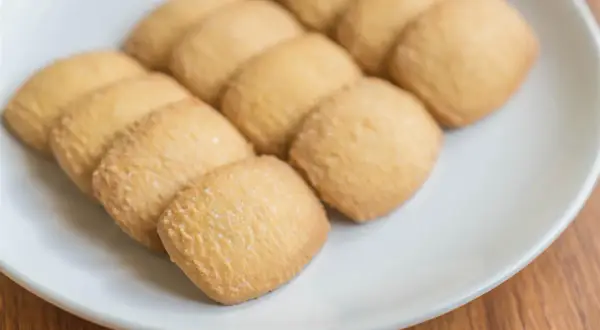 Na białym talerzu ułożone są złociste kocie języczki, posypane cukrem.