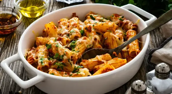 Pyszny obiad z mięsa mielonego: makaron rigatoni zapieczony z sosem bolońskim i ciągnącym serem, posypany świeżą natką pietruszki.