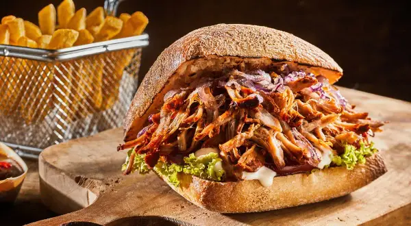 Apetyczny burger z szarpaną wieprzowiną, chrupiącymi frytkami i świeżą sałatą na drewnianej desce.