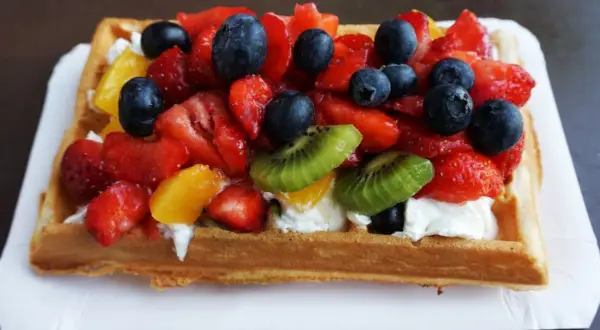 Pyszne gofry z bitą śmietaną i mnóstwem świeżych owoców: truskawek, borówek, kiwi i brzoskwiń.