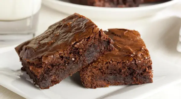 Dwa wilgotne brownie z nutellą, posypane solą morską, na białym talerzyku.