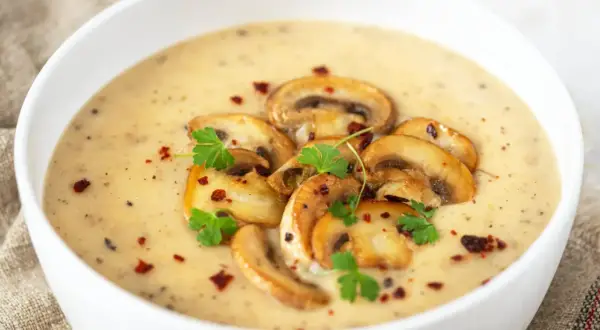 Aksamitny zupa krem z pieczarek, udekorowana plasterkami pieczarek, natką pietruszki i płatkami chili.