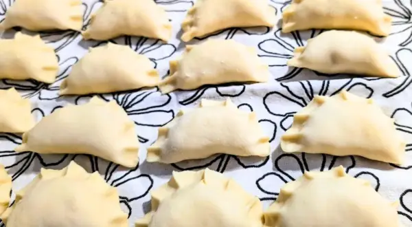 Rządki surowych, gotowych do gotowania, **weganskich pierogów** ułożonych na białym materiale z czarnymi, abstrakcyjnymi wzorami.