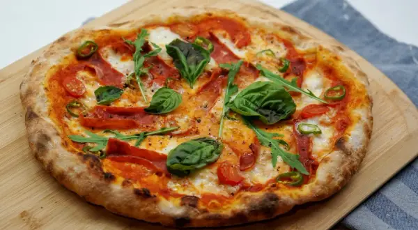 Pyszna pizza z rukolą, pomidorkami, papryczką i wędliną. Idealne dodatki do pizzy na drewnianej desce.
