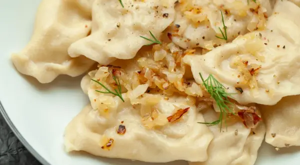 Pyszne pierogi z ziemniakami, okraszone cebulką i koperkiem, posypane pieprzem.