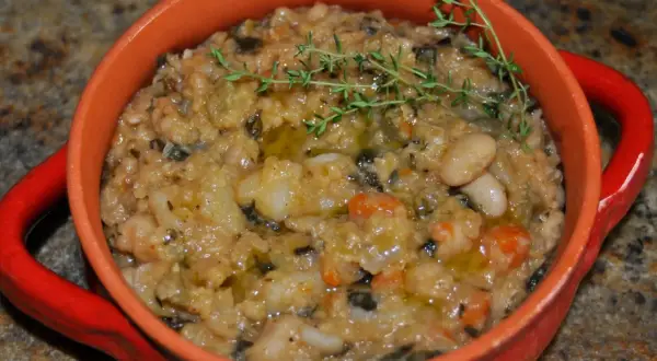 Gęsta, sycąca zupa ribollita z fasolą, warzywami i ziołami, podana w pomarańczowej miseczce.