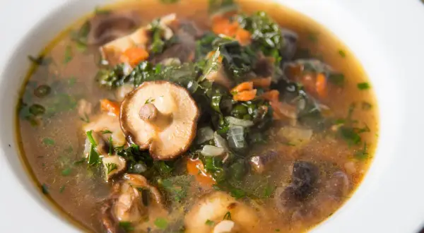 Aromaticzna, tradycyjna zupa grzybowa z kawałkami grzybów shiitake, zielonymi liśćmi i marchewką, podana w białej misce.