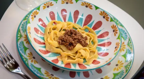 Pyszne tagliatelle al ragu podane w kolorowej miseczce z motywem kwiatowym. Obok leży widelec.