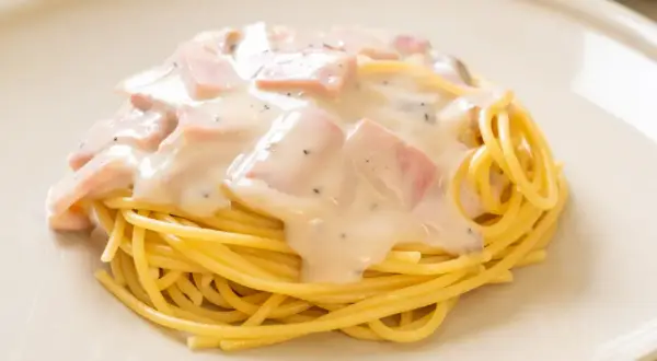 Pyszny makaron z pancettą i kremowym sosem, posypany pieprzem, na jasnym talerzu.