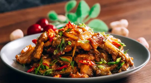 Chrupiąca wieprzowina po chińsku, z papryczkami chili i szczypiorkiem, na szarym talerzu.