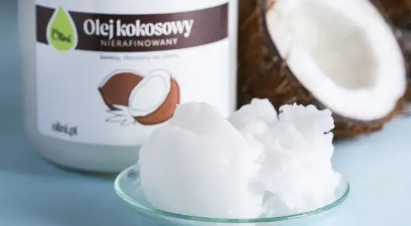Olej kokosowy nierafinowany na talerzyku, idealny jako jaki olej do smażenia. Obok połówka kokosa i słoik z etykietą.