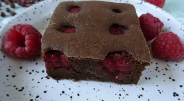 Pyszny fit brownie z fasoli, z malinami w środku i na talerzu. Idealny deser dla łasuchów.